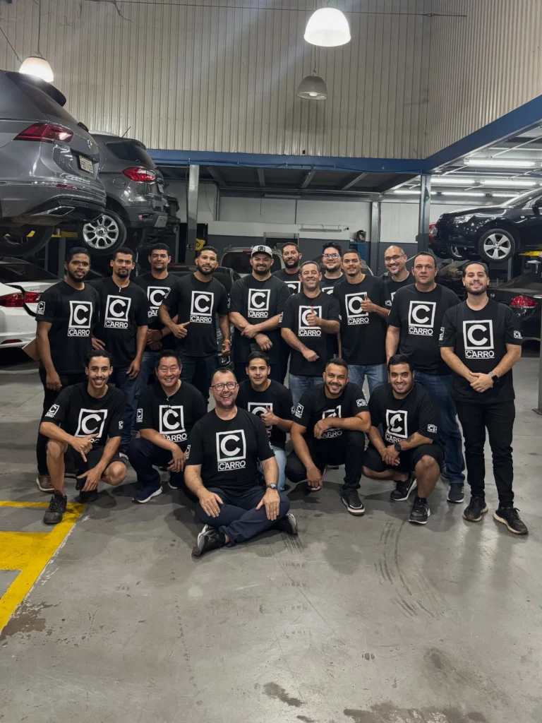 Equipe da oficina mecânica BBX reunida em Brasília, vestindo camisetas pretas com o logotipo da empresa dentro da oficina com carros em elevadores hidráulicos.